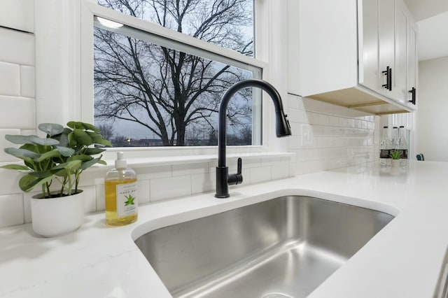 interior details featuring light stone counters, sink, decorative backsplash, and white cabinets