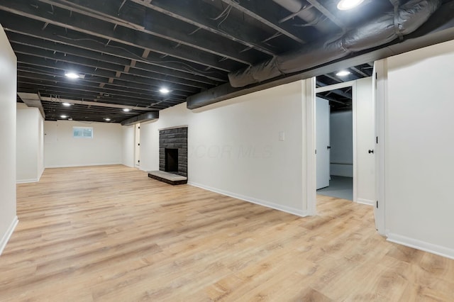 basement with a stone fireplace and light hardwood / wood-style floors