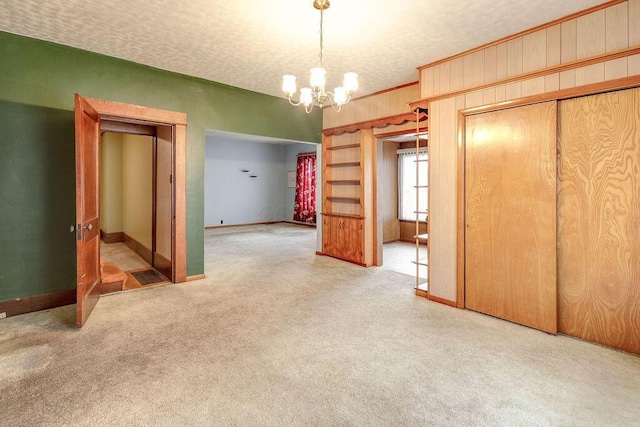 unfurnished bedroom with wood walls, carpet floors, a notable chandelier, a textured ceiling, and a closet