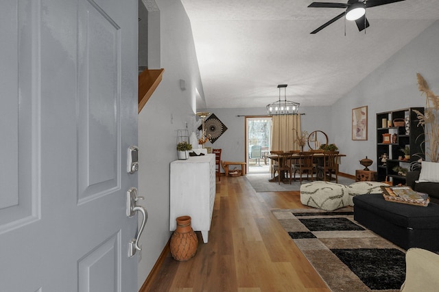 living room featuring lofted ceiling, ceiling fan with notable chandelier, a textured ceiling, and light hardwood / wood-style flooring