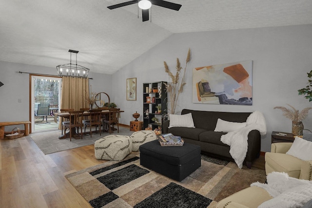 living room with hardwood / wood-style floors, ceiling fan with notable chandelier, vaulted ceiling, and a textured ceiling