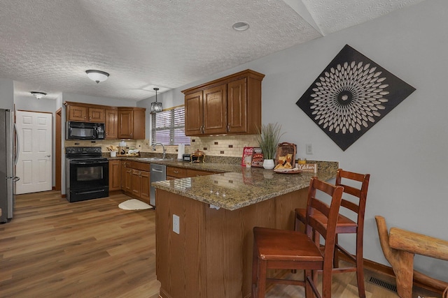 kitchen with wood-type flooring, hanging light fixtures, kitchen peninsula, dark stone counters, and black appliances