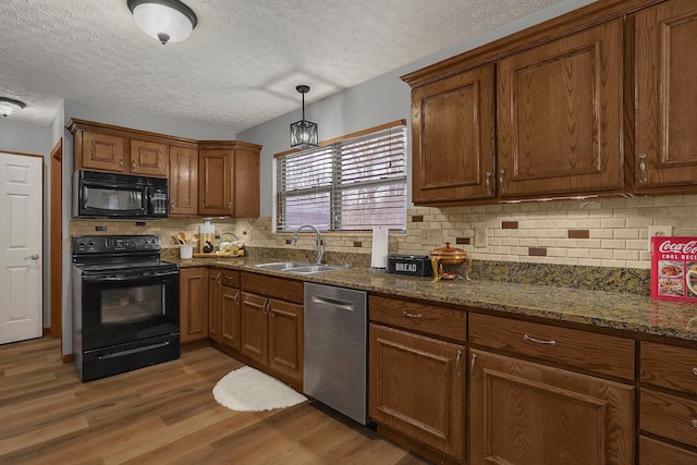 kitchen with sink, wood-type flooring, decorative light fixtures, dark stone counters, and black appliances