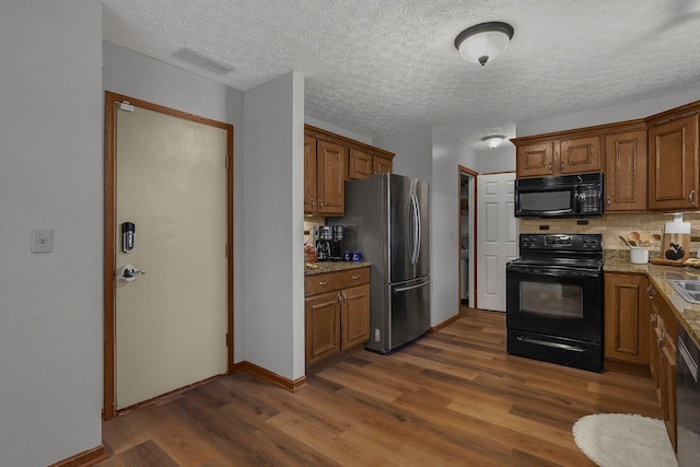 kitchen with dark hardwood / wood-style flooring, light stone countertops, decorative backsplash, and black appliances