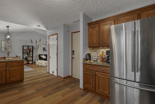 kitchen with tasteful backsplash, hanging light fixtures, dark stone countertops, stainless steel fridge, and dark hardwood / wood-style flooring