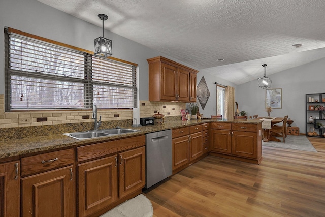 kitchen featuring pendant lighting, sink, dishwasher, vaulted ceiling, and kitchen peninsula