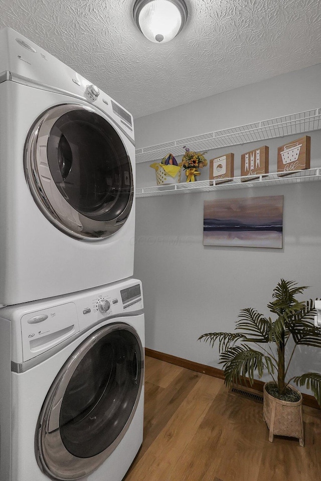 laundry room featuring stacked washer and dryer, hardwood / wood-style floors, and a textured ceiling