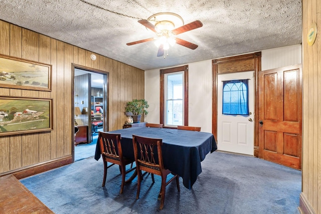 dining area with ceiling fan, wooden walls, a textured ceiling, and carpet