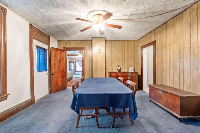 carpeted dining room with a textured ceiling, ceiling fan, and wood walls