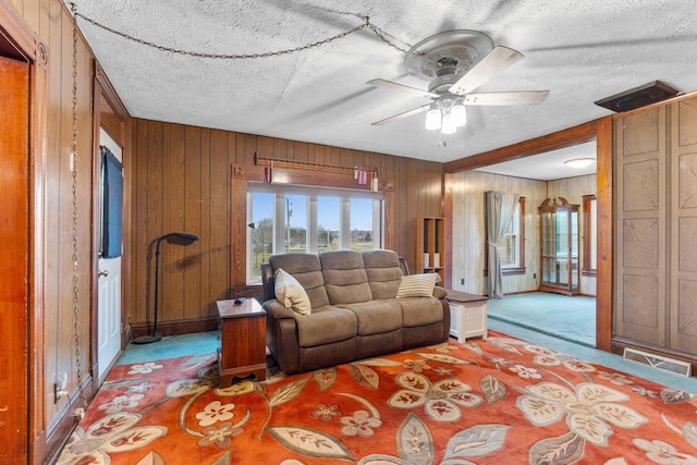 living room featuring ceiling fan, wooden walls, light colored carpet, and a textured ceiling