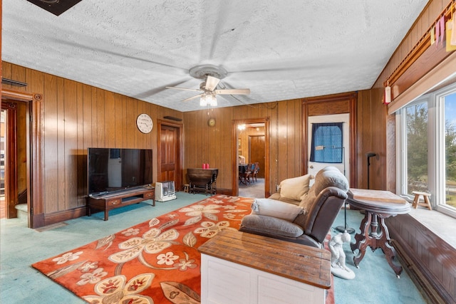 carpeted living room featuring ceiling fan, a textured ceiling, and wood walls