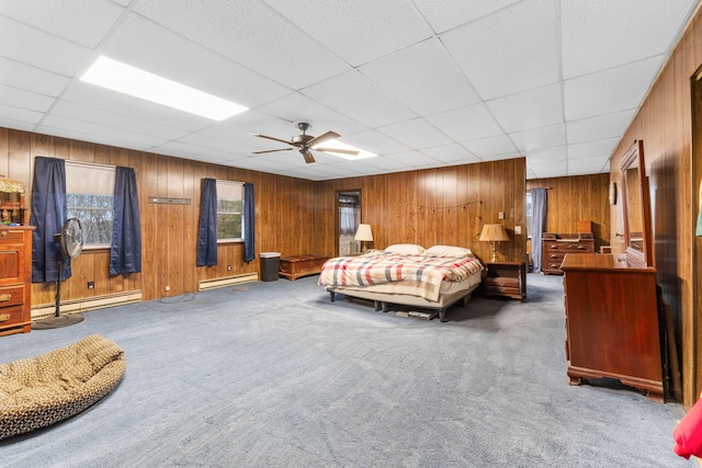 carpeted bedroom featuring baseboard heating, ceiling fan, a drop ceiling, and wood walls