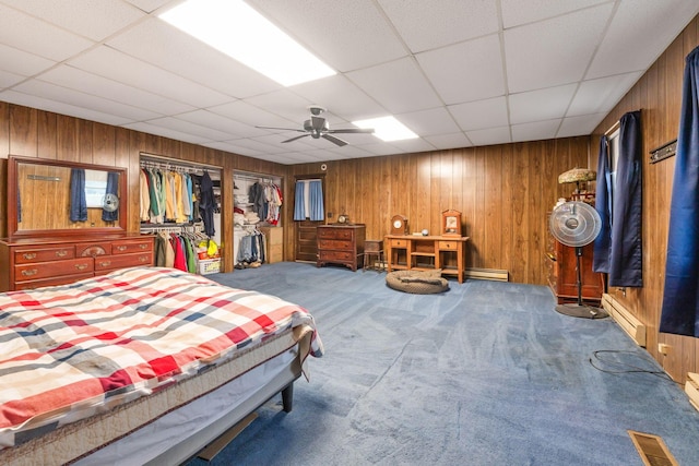 bedroom with wooden walls, a baseboard radiator, ceiling fan, and carpet flooring