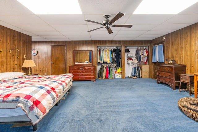 bedroom featuring ceiling fan, carpet flooring, wooden walls, and a paneled ceiling