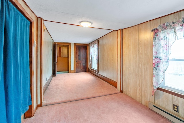 empty room featuring wood walls, light colored carpet, and a baseboard heating unit