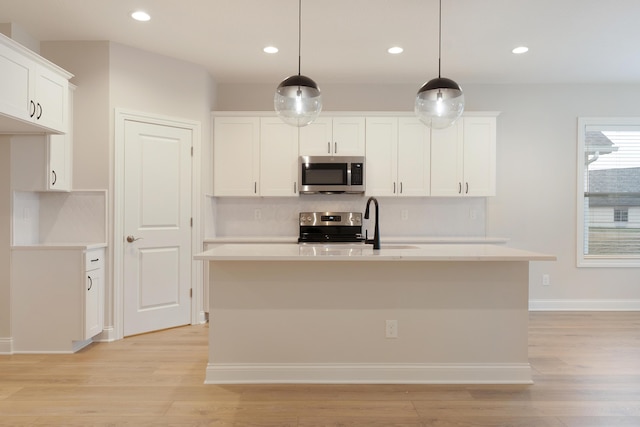 kitchen featuring appliances with stainless steel finishes, decorative light fixtures, an island with sink, and white cabinets