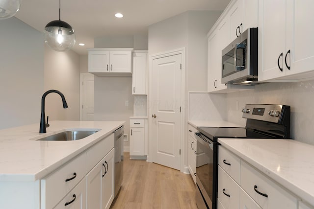 kitchen featuring sink, appliances with stainless steel finishes, white cabinetry, decorative light fixtures, and light wood-type flooring