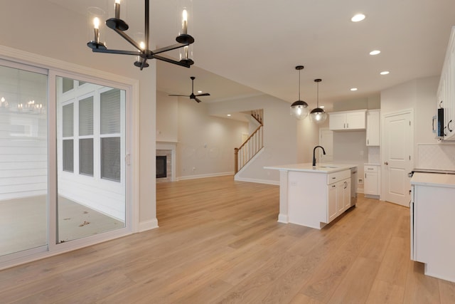 kitchen featuring appliances with stainless steel finishes, a kitchen island with sink, hanging light fixtures, white cabinetry, and light wood-type flooring