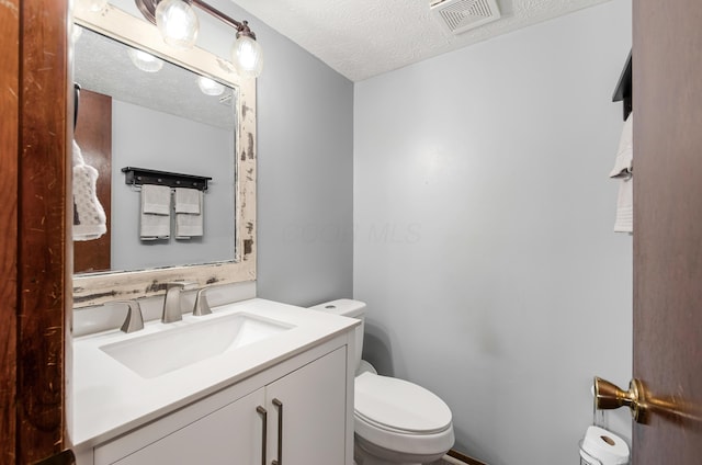 half bathroom with visible vents, a textured ceiling, toilet, and vanity