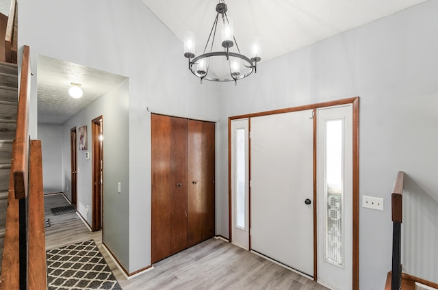 foyer entrance featuring baseboards, a notable chandelier, a textured ceiling, and light wood finished floors