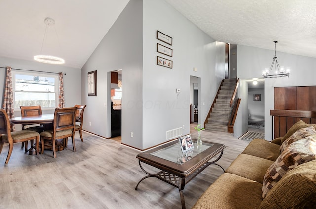 dining room with a textured ceiling, visible vents, stairway, light wood-type flooring, and an inviting chandelier