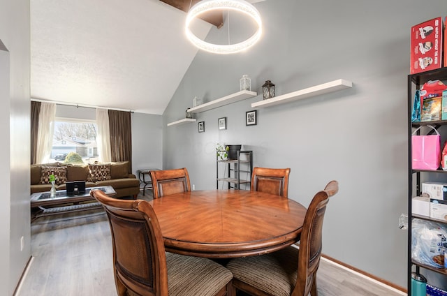 dining space with vaulted ceiling, a textured ceiling, baseboards, and wood finished floors