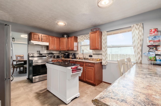 kitchen with appliances with stainless steel finishes, brown cabinetry, a sink, a kitchen island, and under cabinet range hood