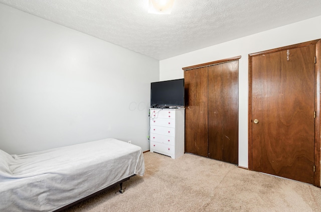 bedroom featuring a textured ceiling, two closets, and light colored carpet