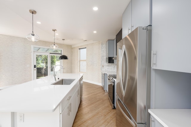 113 E Mithoff St, Columbus, OH 43206 - kitchen with appliances with stainless steel finishes, a center island with sink, light wood-type flooring, light countertops, and hanging light fixtures