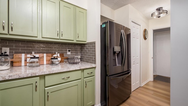 kitchen with backsplash, green cabinets, light hardwood / wood-style floors, stainless steel fridge with ice dispenser, and light stone countertops