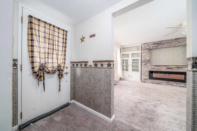 bathroom featuring a textured ceiling, wainscoting, ceiling fan, a stone fireplace, and built in shelves