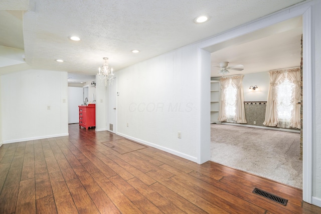 empty room with ceiling fan with notable chandelier, a textured ceiling, visible vents, and wood finished floors