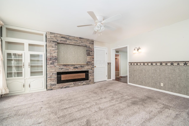 unfurnished living room with carpet, a fireplace, ceiling fan, a wainscoted wall, and built in shelves