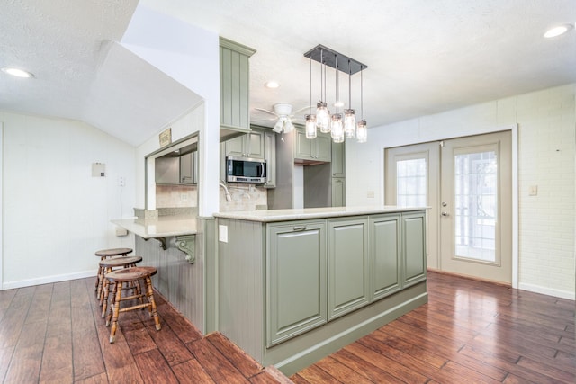 kitchen with light countertops, a peninsula, stainless steel microwave, and dark wood finished floors