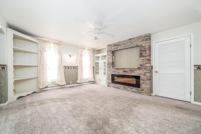 unfurnished living room with a fireplace, built in shelves, a ceiling fan, and carpet floors