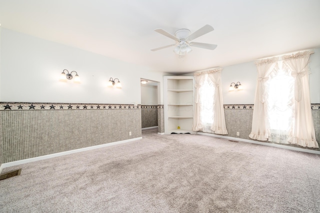 unfurnished room with visible vents, a wainscoted wall, wallpapered walls, carpet floors, and a ceiling fan