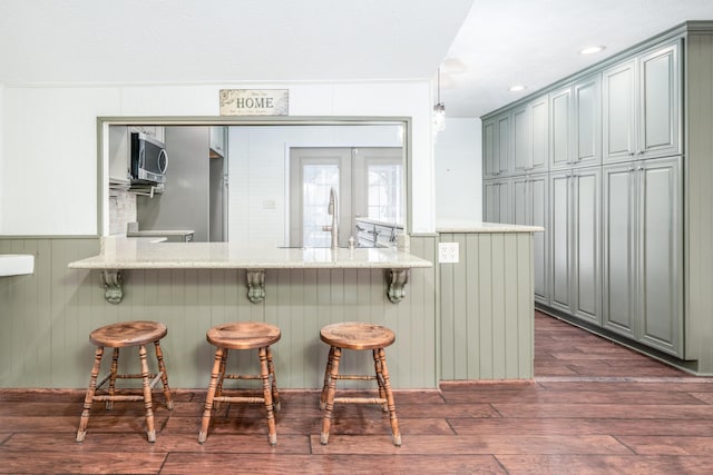 kitchen featuring a sink, stainless steel microwave, dark wood-type flooring, a kitchen breakfast bar, and a peninsula