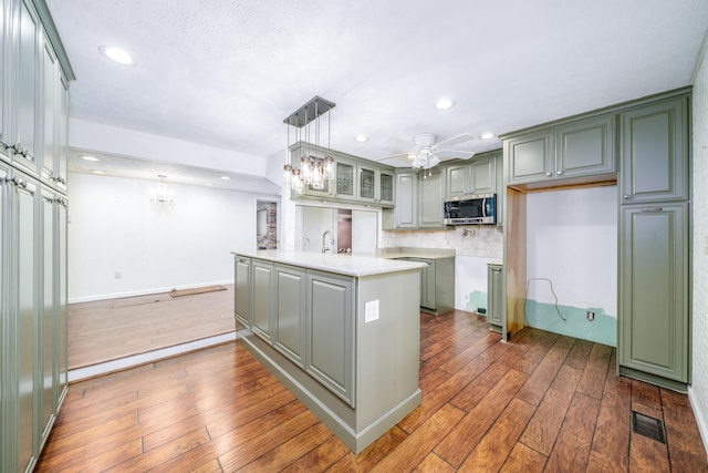 kitchen featuring hanging light fixtures, glass insert cabinets, light countertops, stainless steel microwave, and a peninsula