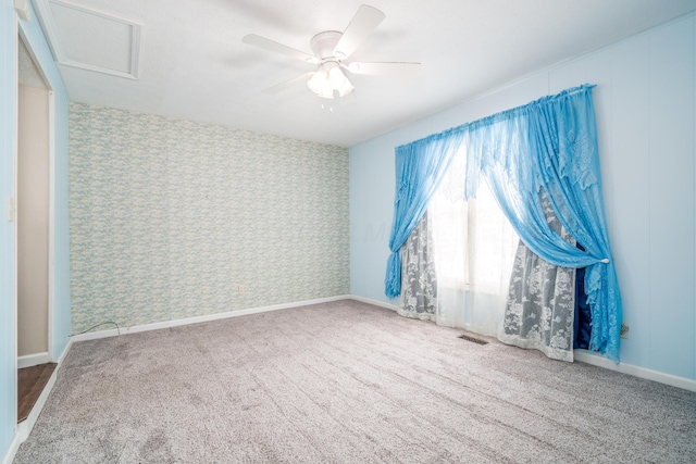 carpeted empty room with ceiling fan, visible vents, baseboards, wallpapered walls, and attic access