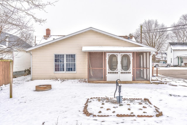 snow covered house featuring a chimney and a sunroom