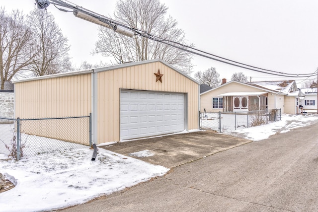 snow covered garage featuring fence and a detached garage