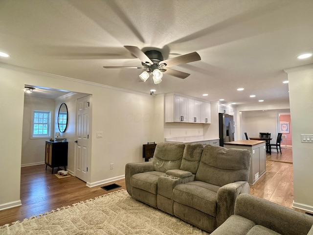 living room featuring crown molding, ceiling fan, and light wood-type flooring