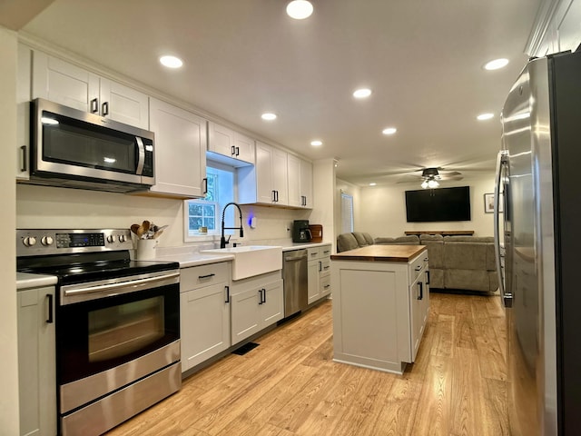 kitchen with sink, light hardwood / wood-style flooring, stainless steel appliances, white cabinets, and a kitchen island