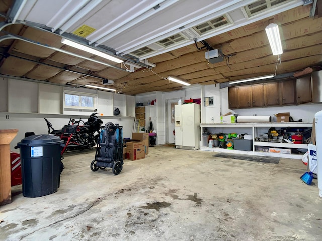 garage with a garage door opener and white refrigerator with ice dispenser