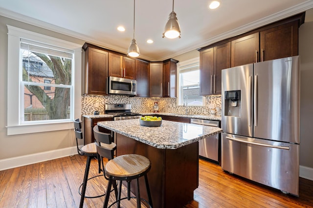 kitchen with a breakfast bar, light stone counters, a kitchen island, pendant lighting, and stainless steel appliances