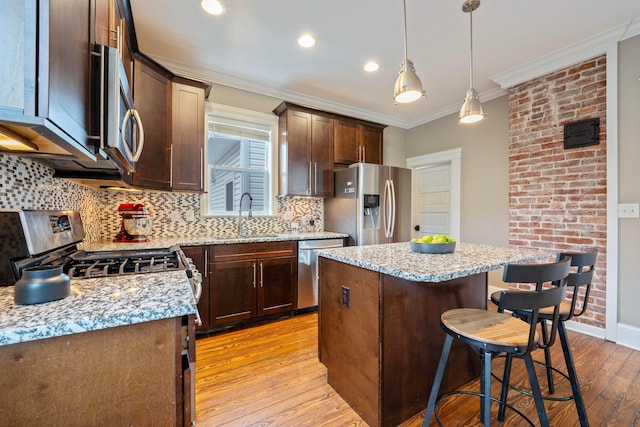 kitchen with sink, a center island, hanging light fixtures, appliances with stainless steel finishes, and light stone countertops