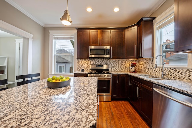 kitchen with sink, appliances with stainless steel finishes, ornamental molding, light stone countertops, and dark hardwood / wood-style flooring