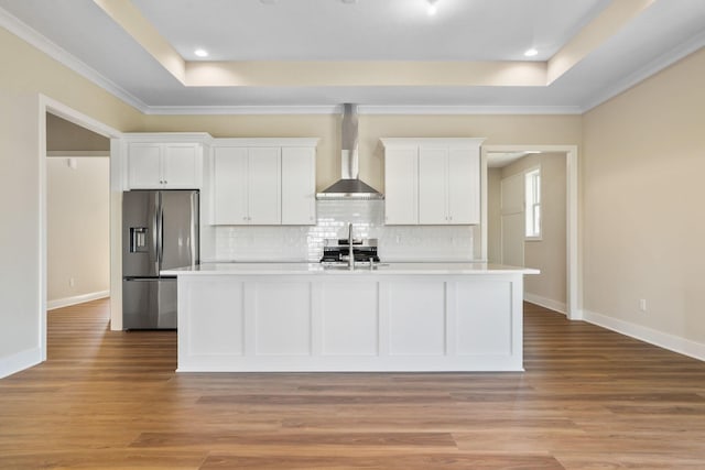 kitchen with stainless steel appliances, a tray ceiling, light countertops, and wall chimney exhaust hood