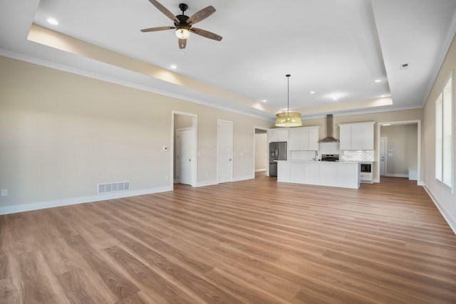 unfurnished living room with visible vents, a raised ceiling, a ceiling fan, baseboards, and light wood-style flooring