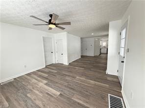 unfurnished living room featuring dark wood-type flooring, ceiling fan, and a textured ceiling